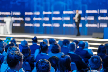 Audience attentively listening to keynote speaker at a corporate event. Blurred conference...