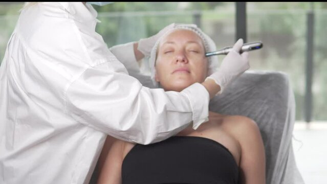 Professional qualified beautician standing next to client during hydrafacial procedure