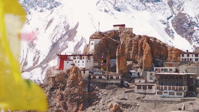 Handheld shot of Dhankar monastery in front of snow covered Himalayas at Spiti Valley in Himachal Pradesh, India. Defocused Buddhist prayer flag waves in front of the Dhankar Gompa during the day.