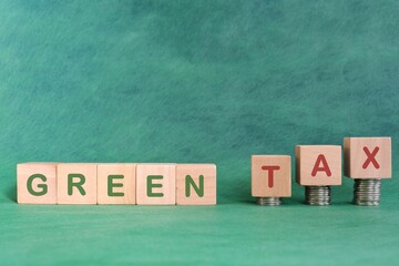 Green and environmental tax concept. Word in wooden blocks with increasing stack of coins.	