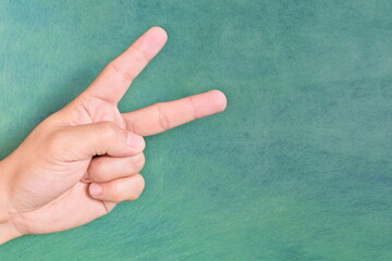 Young male Asian hand making peace sign or letter v sign isolated on green background.