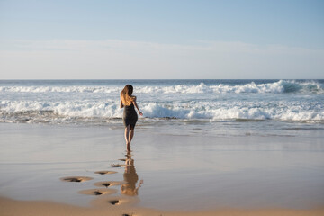 Mujer joven con pelo largo corriendo hacia la playa dejando huellas en cada paso que da. Diversión de verano.