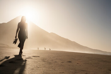 Silueta de una mujer joven disfrutando de una tranquila caminata al atardecer en la suave arena....