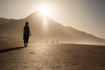 Silueta de una mujer joven disfrutando de una tranquila caminata al atardecer en la suave arena. Serenidad, naturaleza, puesta de sol, bienestar. - obrazy, fototapety, plakaty
