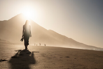 Silueta de una mujer joven disfrutando de una tranquila caminata al atardecer en la suave arena....