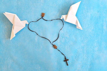 White dove origami carrying rosary or scapular in sky blue background.