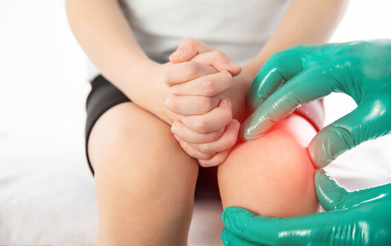 A doctor traumatologist orthopedist examines the knee joint of a child who has knee pain. Concept of growing pains in children. Dislocation and injury of the knee, sprain, hypothermia