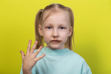 A seven-year-old caucasian girl with a mouth dirty from chocolate on a yellow background. Concept of children with sweet tooth, blood sugar level, diabetes and calories. Junk food. Caries on teeth