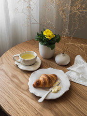 Delicious simple breakfast, snack - green tea, croissant, butter on a wooden round table