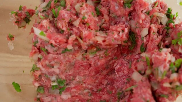Macro filming, the chef uses a spoon to mix meat, minced beef with onions and herbs in a glass bowl. Close-up, top view, macro