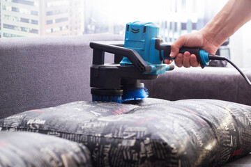 Dry cleaning of the sofa with a special electric brush to raise the pile, close-up. - obrazy, fototapety, plakaty