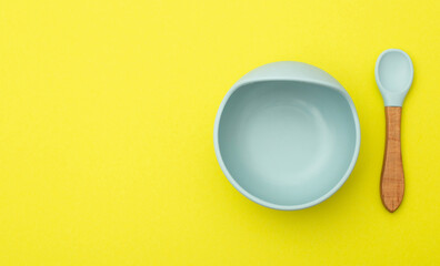 Silicone baby plate and spoon on a yellow background. The concept of feeding babies with cereals...