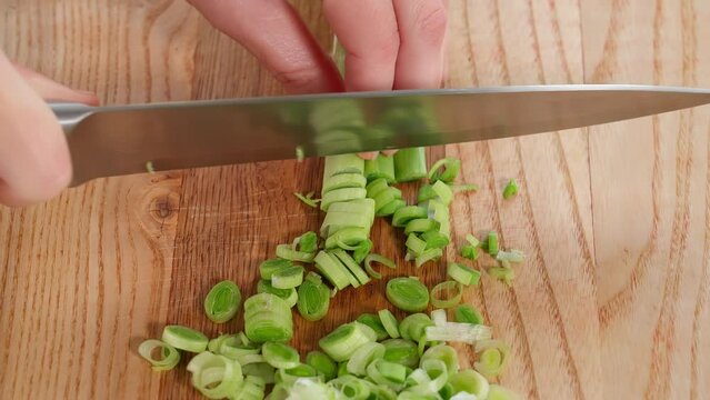 The chef in the kitchen prepares a healthy salad, chops leeks on a wooden board. Close-up, side view, macro
