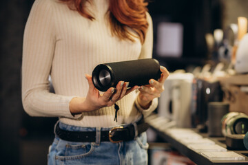 a woman chooses a bluetooth speaker in an electronics store