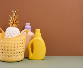 Brightly colored composition with laundry detergents and decoarative pineapple in a yellow laundry basket. Copy space for text.