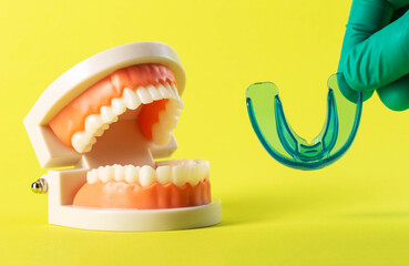 Dental mouthguard and cofferdam in the hand of a dentist doctor against the background of a mock-up of a dental jaw on a yellow background. Concept for the treatment of bruxism