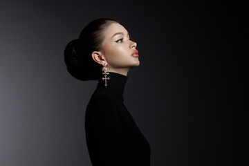 Profile of a graceful woman in a black turtleneck, adorned with ornate cross earrings, exuding...