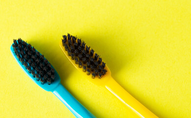 Two toothbrushes with black charcoal hard bristles on a yellow background, close-up. The concept of...