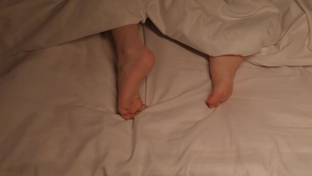 restless feet of a kid boy on a sheet under a blanket at night. Baby child girl with bare legs tosses and does not fall asleep in bed in the bedroom in the evening