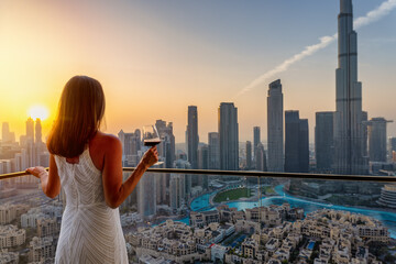 A beautiful woman enjoys the panoramic sunset view over the skyline of Downtown Dubai, UAE, with a...