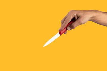 Black male hand holding a red cooking knife isolated on yellow background.