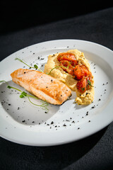 Close-up of salmon steak with hummus and tomatoes on a white plate