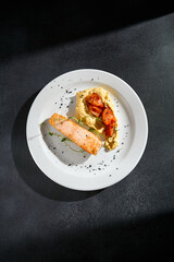 Top view of salmon steak with hummus and tomatoes on a white plate