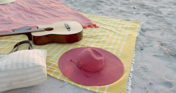A guitar and a pink hat rest on a beach blanket, with copy space