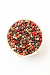 Mix of dry peppercorns in bowl on a white background. Red, black, white and green peppercorns