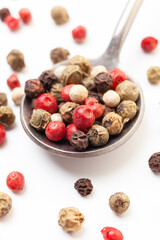 Pepper mix of red, black, white and green peppercorns in iron spoon on white background. Organic spice