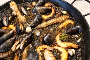 Paella in large frying pan black rice fresh from the restaurant's kitchen with rice, shrimps,...