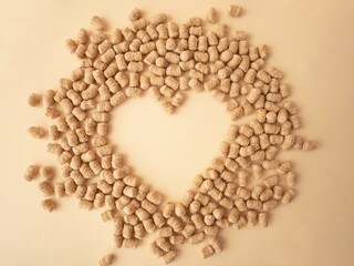 Extruded wheat bran is scattered over a beige background forming a heart-shaped blank space for text. The concept of proper snacking, nutrition and weight loss