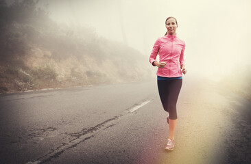 Fototapeta premium Nature, health and woman running in fog on mountain road for race, marathon or competition training. Sports, exercise and athlete with cardio workout for fitness in misty outdoor woods or forest.