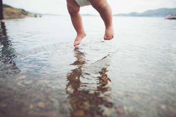 A baby is playfully jumping into the liquid with a diaper on at the beach
