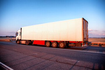 A truck with a refrigerated semi-trailer transports perishable food products in the evening against...