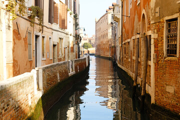 Fototapeta na wymiar Typical narrow streets and canals between сolorful and shabby houses in Venice, Italy. Historical architecture in Venice, parked boats on the canals.