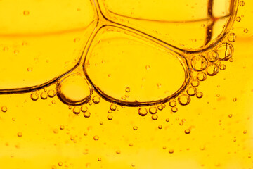 Golden yellow abstract oil bubbles or face serum background. Oil and water bubbles macro photography.