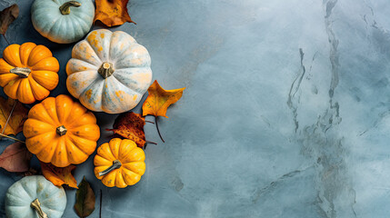 A group of pumpkins with dried autumn leaves and twig, on a light blue color marble - obrazy, fototapety, plakaty