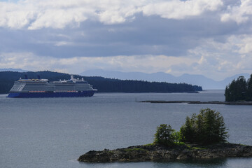 Breathtaking mountain glacier range view with luxury cruiseship cruise ship liner Solstice sailing in front of Alaska mountains departure from Ketchikan with spectacular landscape scenery