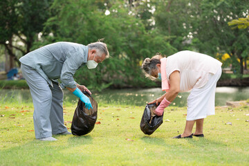 senior couple volunteer wearing face mask holding garbage bag and cleaning in the park