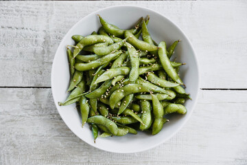 Edamame salted green soybeans in bowl on white wooden table with space for text. Top view.
