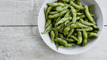 Edamame salted green soybeans in bowl on white wooden table with space for text. Top view.
