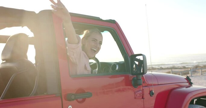 Young Caucasian woman enjoys a sunny beach drive in a red jeep on a road trip