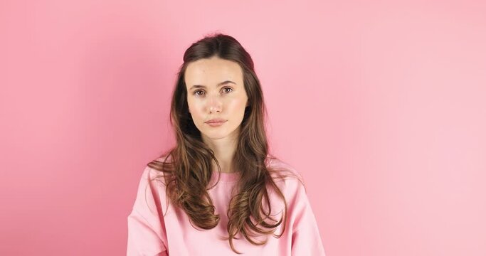 Displeased brunette haired woman showing silence gesture in pink studio background, shh gesture. Girl wear pink long sleeves look by side, she is mad and angry.