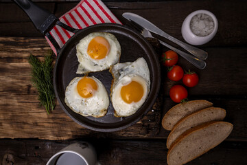 Fried eggs in a pan with vegetables and herbs on a black background.