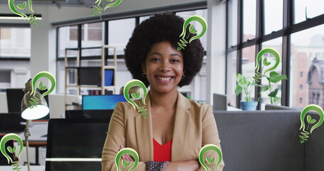 Image of lightbulb icons over smiling african american businesswoman in office