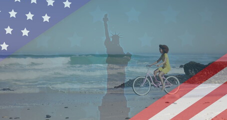 Image of american flag revealing statue of liberty and woman riding bike on beach