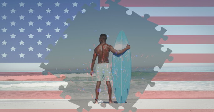 Image of american flag jigsaw puzzles revealing confetti and man with surfboard on beach - Powered by Adobe
