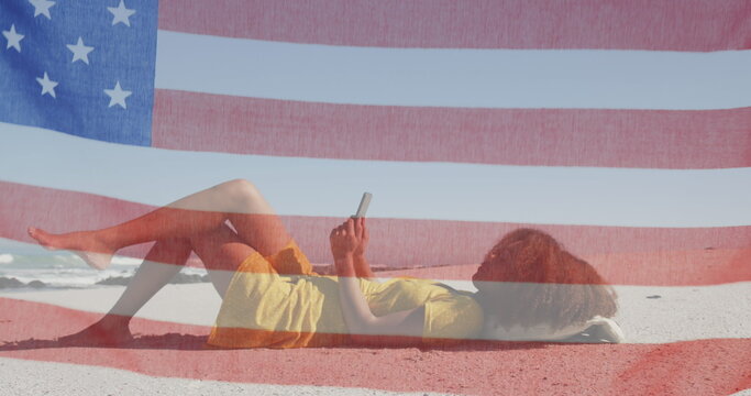 Image of american flag waving over woman using tablet lying on beach