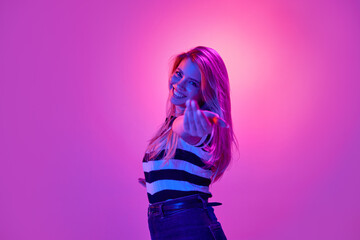 Portrait of beautiful young woman with pretty smile, smiling, posing against pink studio background in neon light. Happiness, attraction. Concept of human emotions, youth, fashion, expression